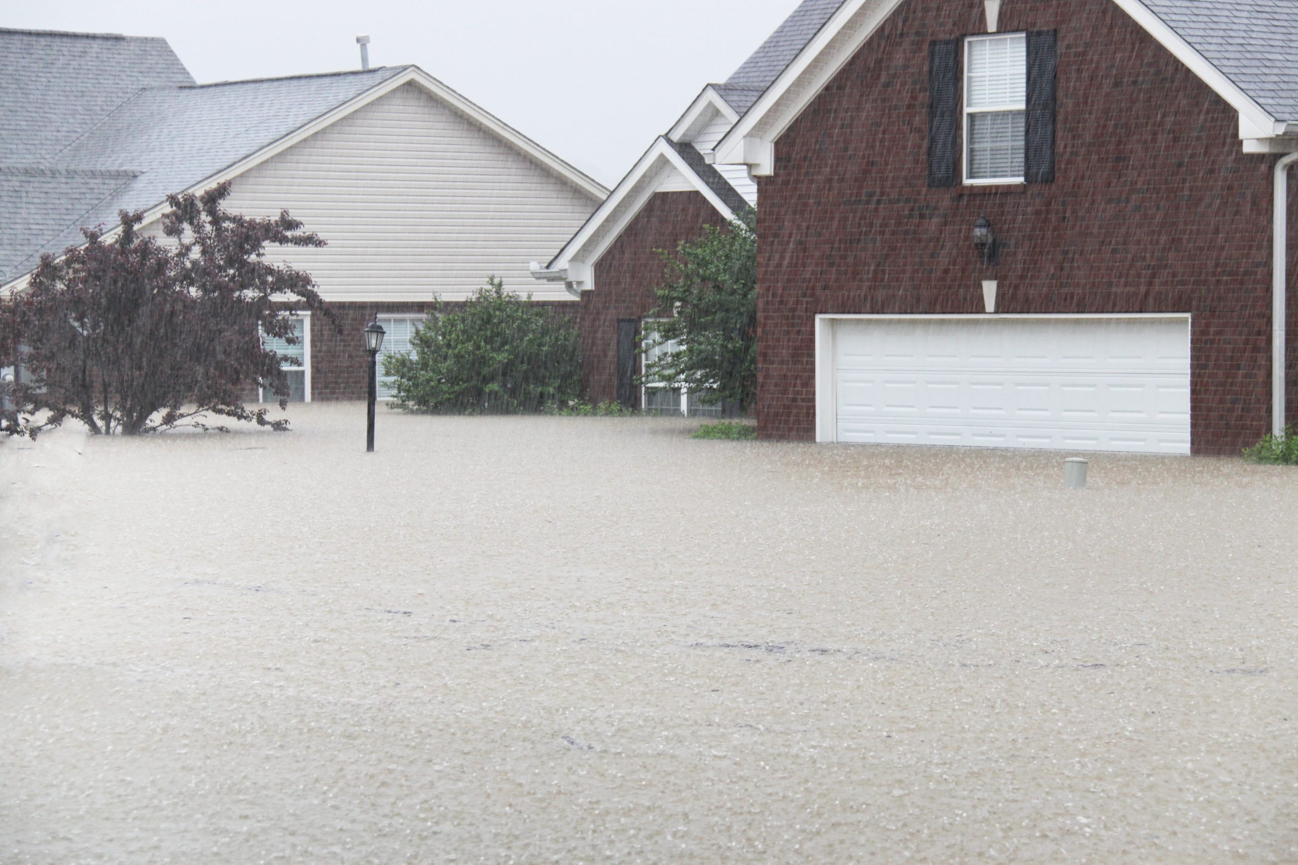 Severe flooding in a residential neighborhood, with houses partially submerged in floodwater during heavy rainfall.