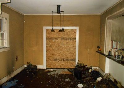 Dining room after a fire with debris everywhere and a boarded up entry