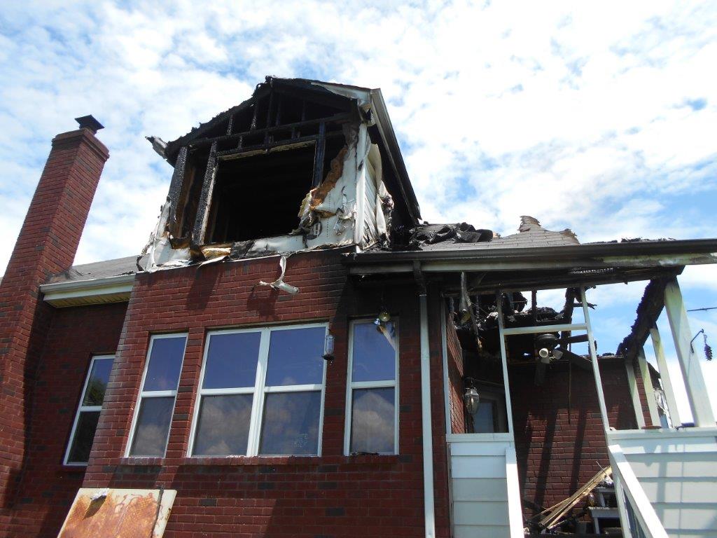 A house with fire damage. The roof is partially collapsed and there is a large hole in the side of the house.