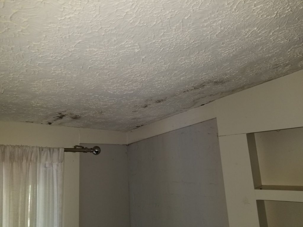 Severe brown water stains and sagging drywall on a ceiling caused by storm-related roof leaks.