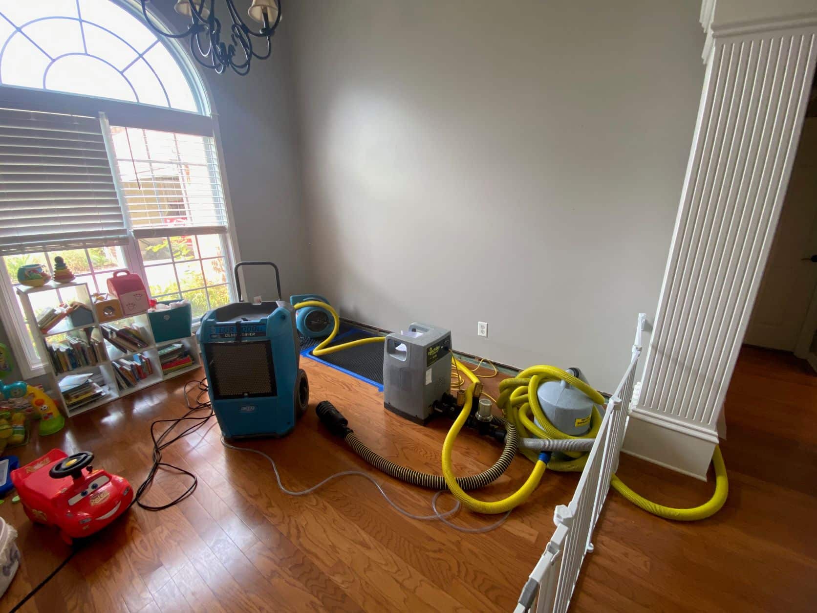 A room with a blue air dryer, gray water extractor and yellow hoses on wooden floor.