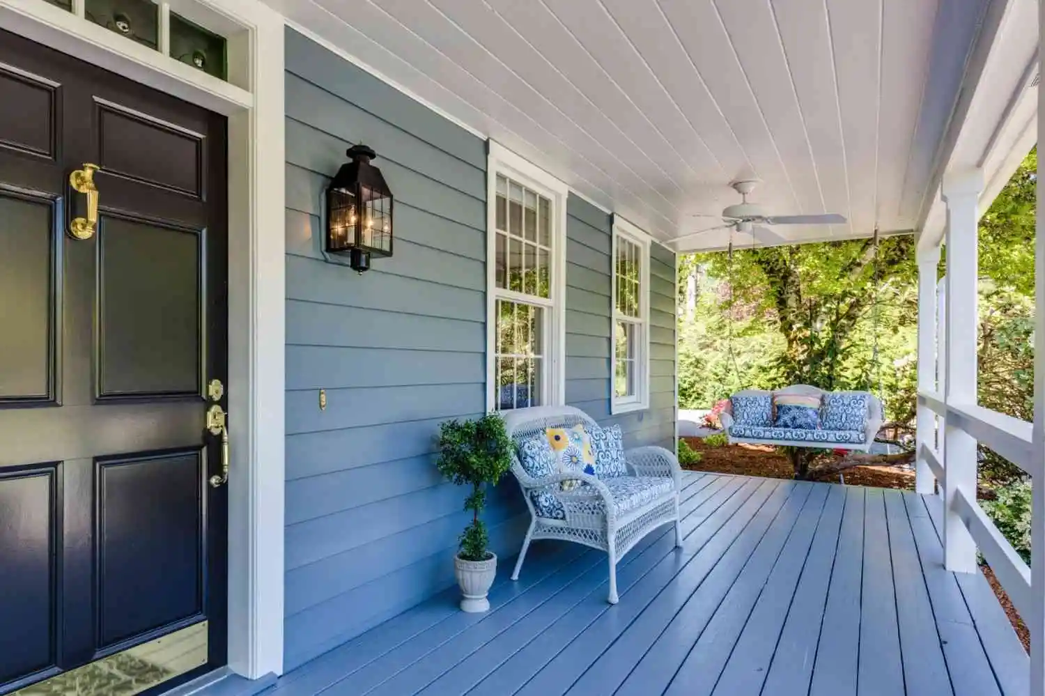 Cozy front porch with blue siding and wicker furniture, reflecting professional home maintenance.