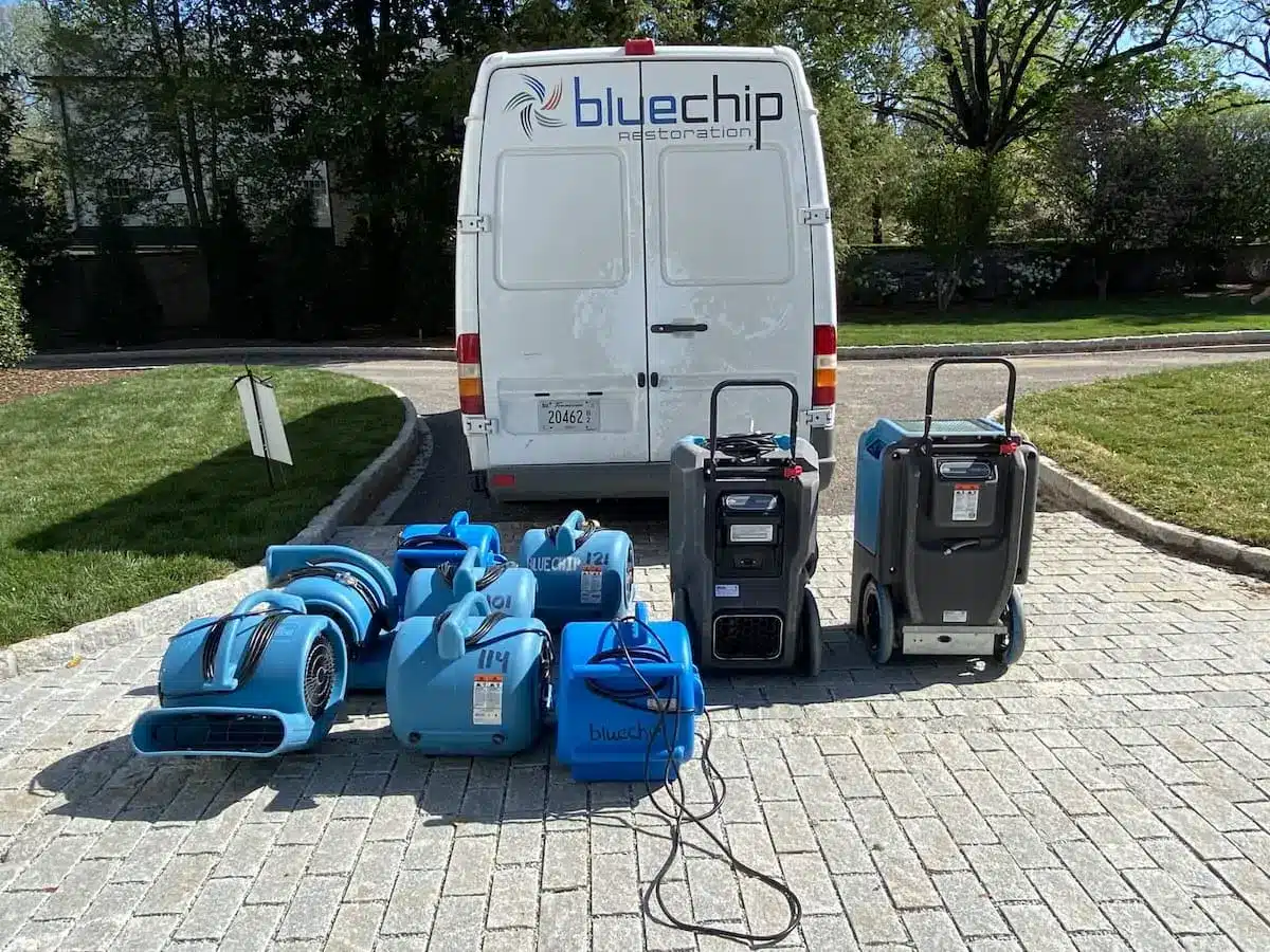 Air movers and dehumidifiers set out in front of a Blue Chip Restoration van for water damage restoration work.