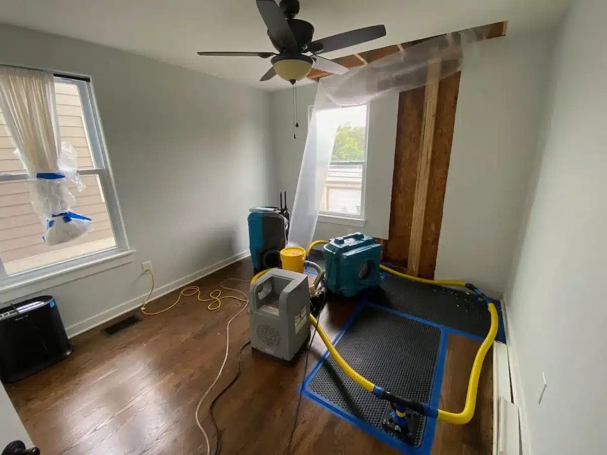 Floor drying mats and drying equipment set up in a room with an opened ceiling and wall during nashville water damage restoration.
